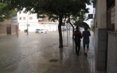 jovenes bajo el paraguas junto a una avenida anegada de denia durante un episodio de lluvia torrencial