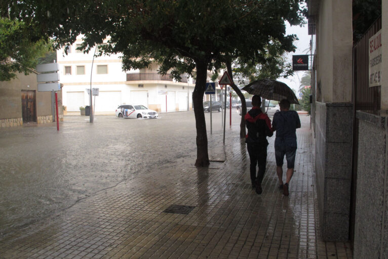 Jóvenes bajo el paraguas junto a una avenida anegada de Dénia durante un episodio de lluvia torrencial